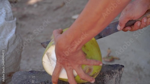 Hand of a man peel green young coconut using machete to make young coconut drink