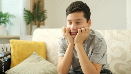 13 years old teen boy watching tv sitting on a couch at home alone.