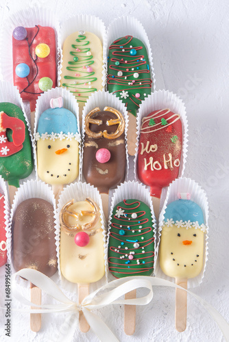Christmas dessert. Sweet food. Cheesecake on a stick in the shape of ice cream. Children's treat in winter. Candy Christmas tree, snowman, deer and Santa Claus. Gingerbread cookies background.