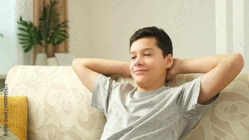 Tired sad teen boy in a gray t shirt sitting on the couch to watch television. Bored boy with hands on head.