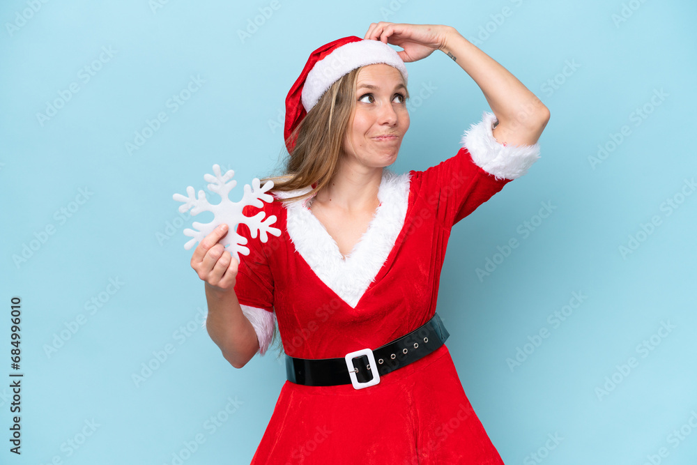 Young caucasian woman dressed as Mama Claus holding a snowflake isolated on blue background having doubts and with confuse face expression Young caucasian woman dressed as Mama Claus holding a snowflake isolated on blue background having doubts and with confuse face expression