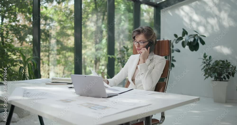 A young woman architect working with invoices and talking on the phone at her work office A young woman architect working with invoices and talking on the phone at her work office