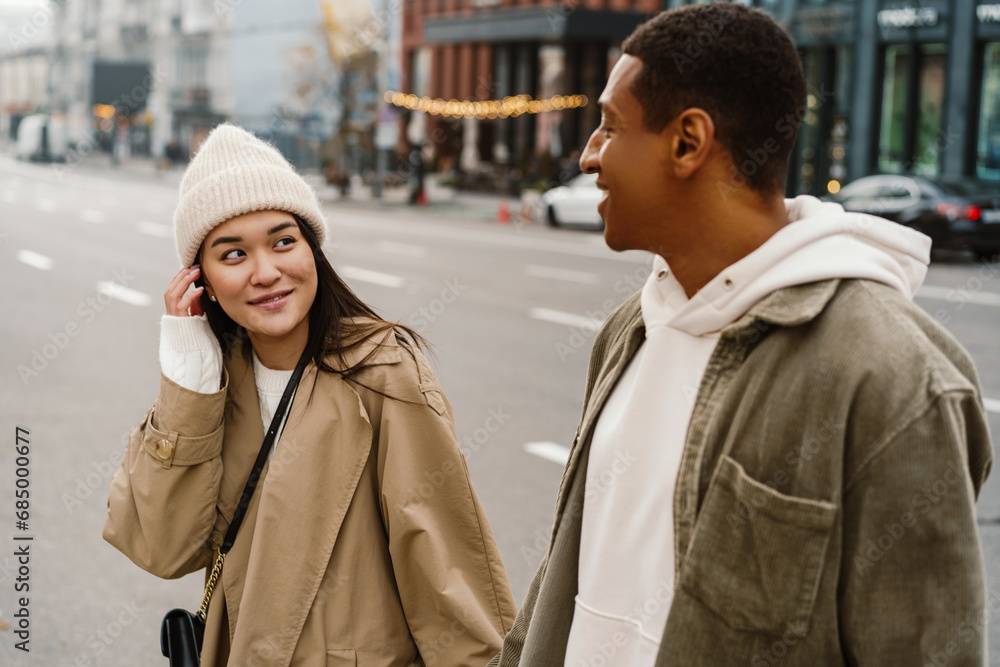 Couple holding hands and looking at each other with smile while walking through city street Couple holding hands and looking at each other with smile while walking through city street