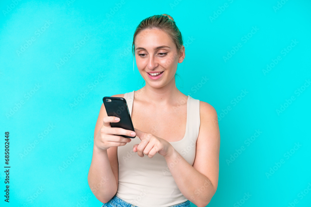 Young caucasian woman isolated on blue background sending a message or email with the mobile Young caucasian woman isolated on blue background sending a message or email with the mobile