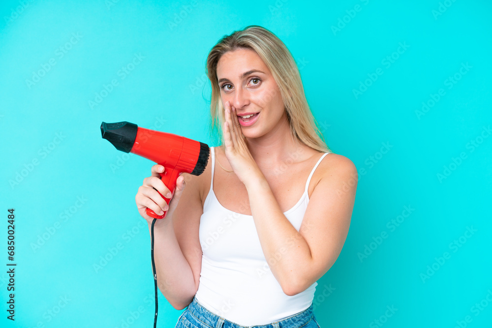 Young caucasian woman holding a hairdryer isolated on blue background whispering something Young caucasian woman holding a hairdryer isolated on blue background whispering something