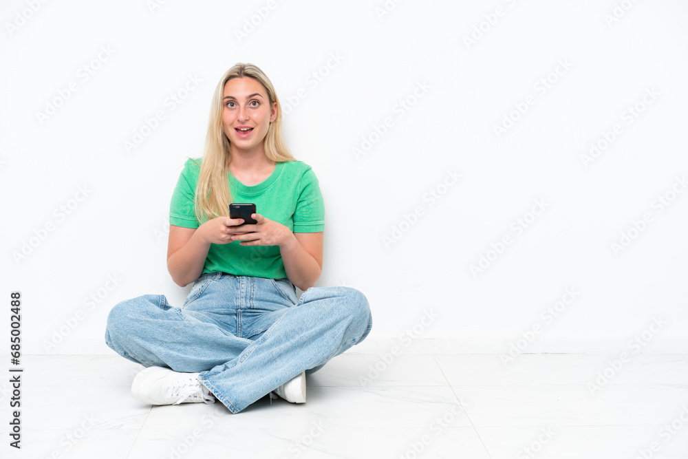 Young caucasian woman sitting on the floor isolated on white background surprised and sending a message Young caucasian woman sitting on the floor isolated on white background surprised and sending a message