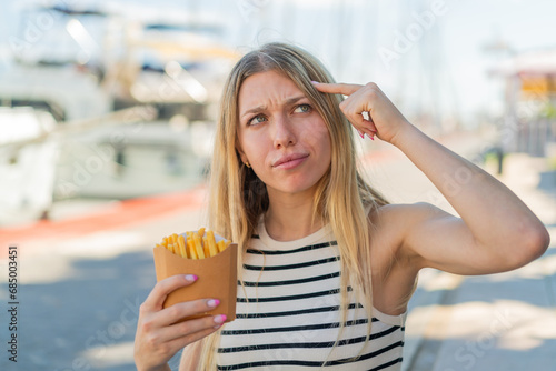 Wallpaper Mural Young blonde woman holding fried chips at outdoors having doubts and with confuse face expression Torontodigital.ca