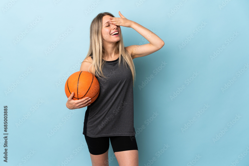 Young blonde woman playing basketball isolated on blue background laughing