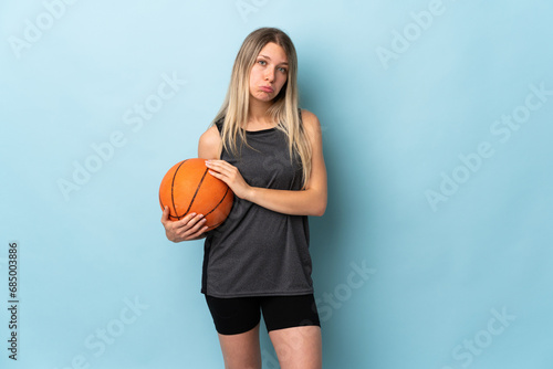 Young blonde woman playing basketball isolated on blue background sad