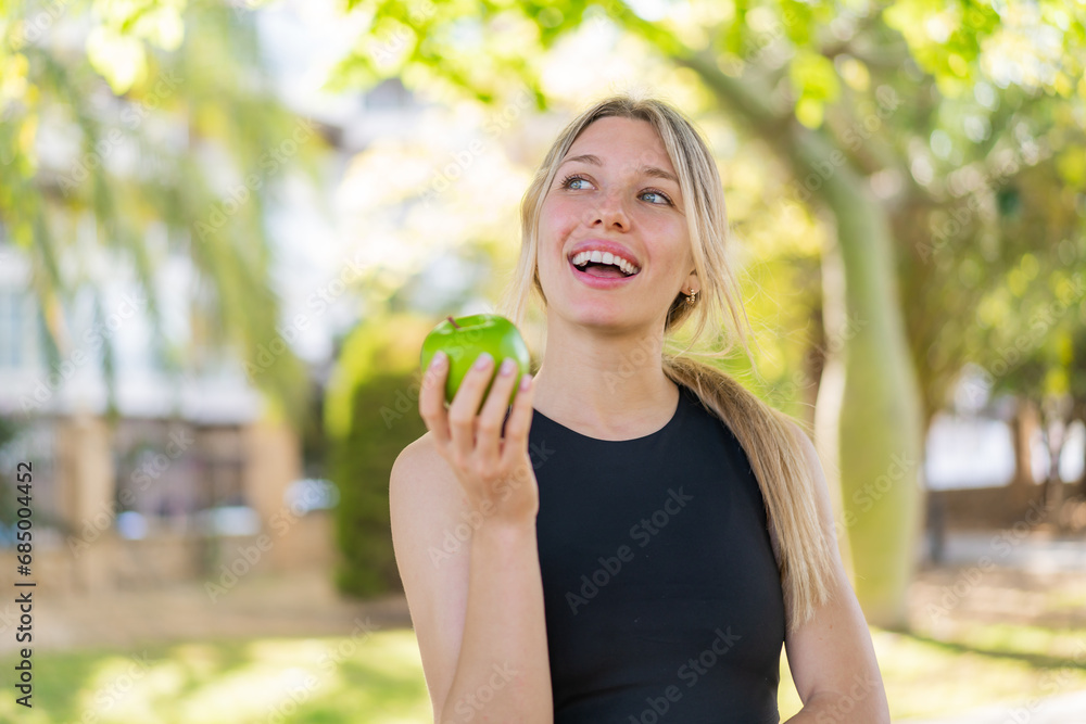 Young blonde woman at outdoors holding an apple with happy expression Young blonde woman at outdoors holding an apple with happy expression
