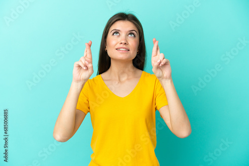 Young caucasian woman isolated on blue background with fingers crossing and wishing the best