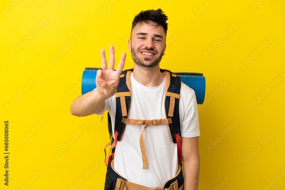 Young mountaineer caucasian man with a big backpack isolated on yellow background happy and counting three with fingers Young mountaineer caucasian man with a big backpack isolated on yellow background happy and counting three with fingers