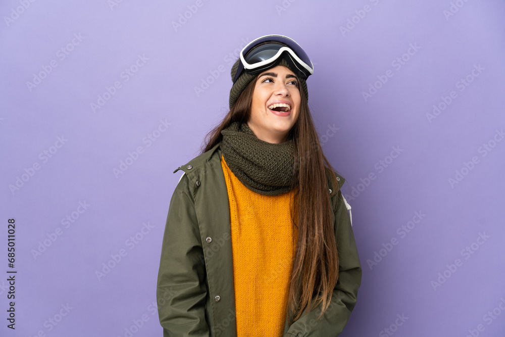 Skier caucasian girl with snowboarding glasses isolated on purple background laughing