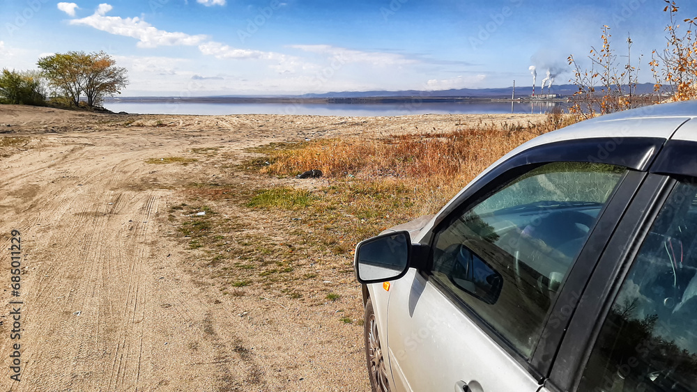 A view of a car on a sandy road and a lake, river or sea in the background. The concept of a summer trip to deserted places