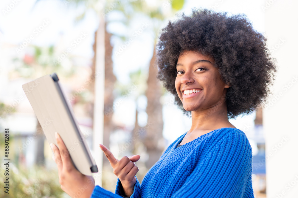 African American girl holding a tablet at outdoors and pointing it African American girl holding a tablet at outdoors and pointing it