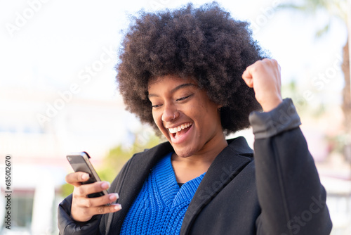 African American girl at outdoors using mobile phone and doing victory gesture