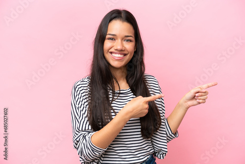Young Colombian woman isolated on pink background surprised and pointing side © luismolinero