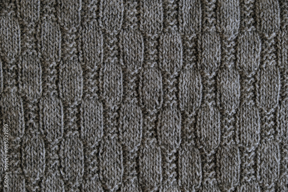 Background with gray knitted leaf shape, knitting pattern with cables. Top view, close-up. Handmade knitting wool Background with gray knitted leaf shape, knitting pattern with cables. Top view, close-up. Handmade knitting wool
