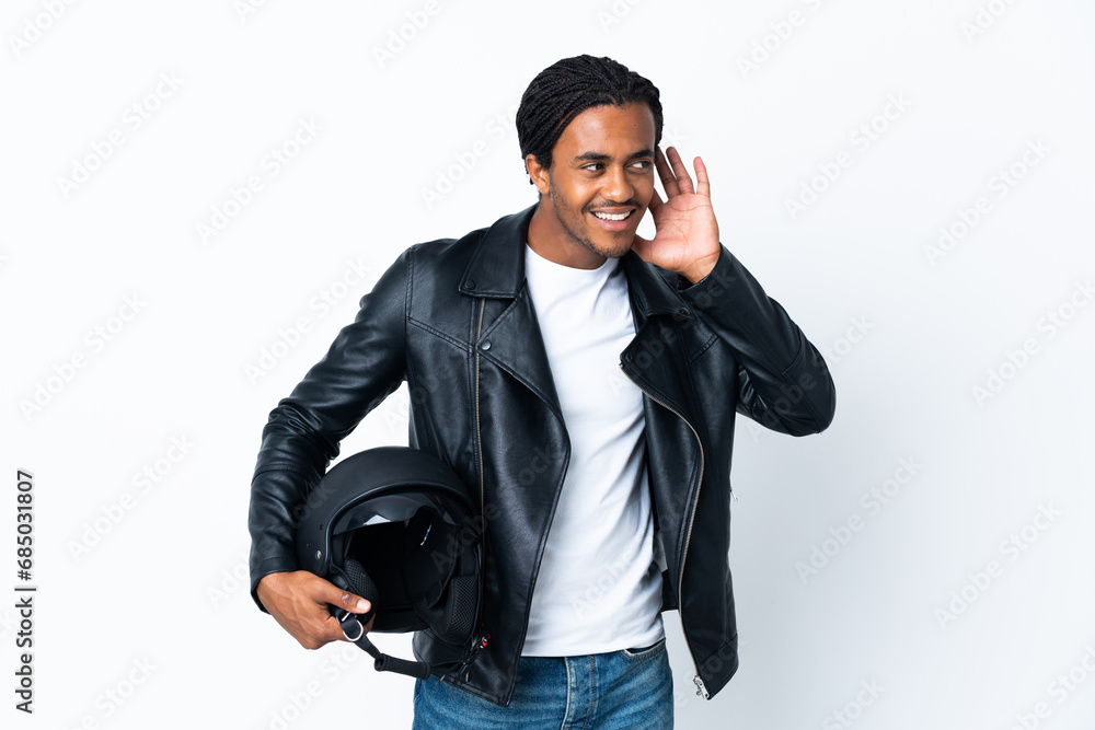African American man with braids holding a motorcycle helmet isolated on white background listening to something by putting hand on the ear African American man with braids holding a motorcycle helmet isolated on white background listening to something by putting hand on the ear