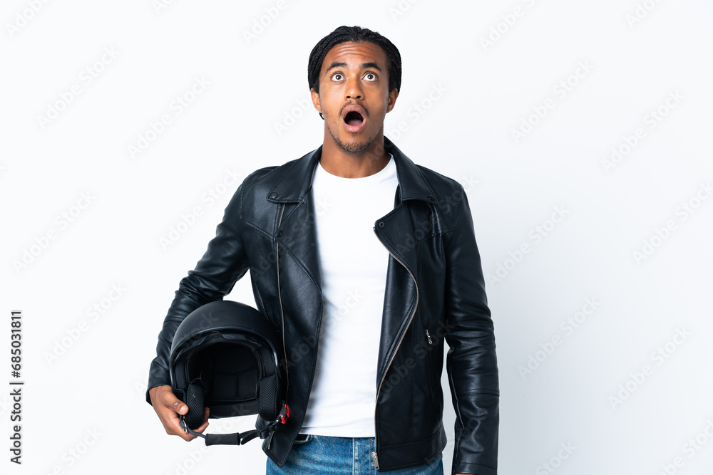 African American man with braids holding a motorcycle helmet isolated on white background looking up and with surprised expression African American man with braids holding a motorcycle helmet isolated on white background looking up and with surprised expression