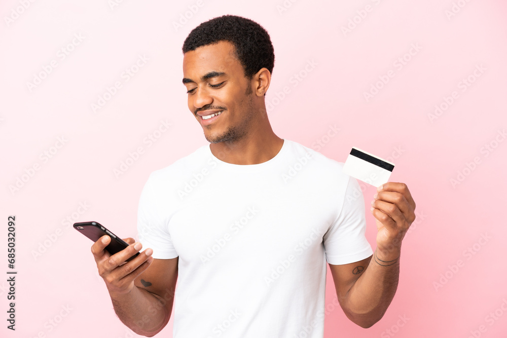 African American handsome man on isolated pink background buying with the mobile with a credit card African American handsome man on isolated pink background buying with the mobile with a credit card
