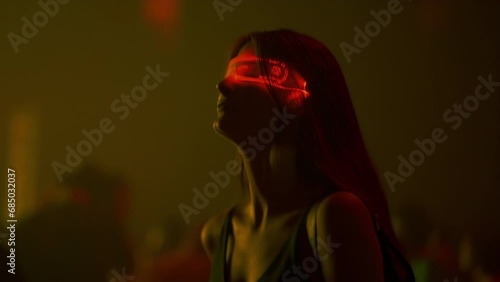 Young woman in futuristic neon glasses at cyberpunk style party in techno club. Sensually dancing girl in glowing goggles moves to music beat in crowd of people. Cyber city nightclub, concept