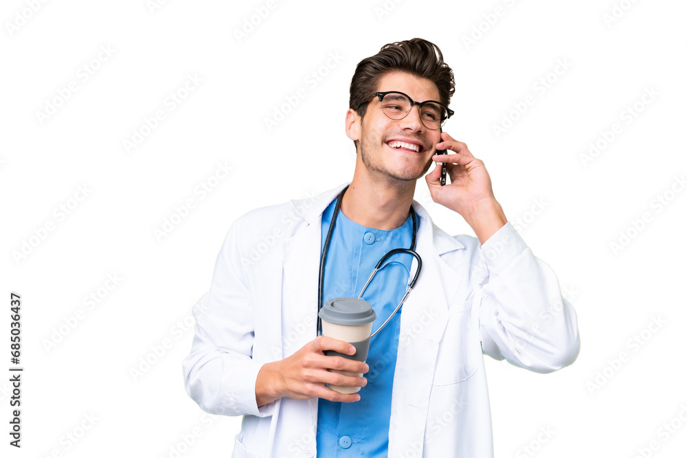 Young doctor man over isolated background holding coffee to take away and a mobile Young doctor man over isolated background holding coffee to take away and a mobile