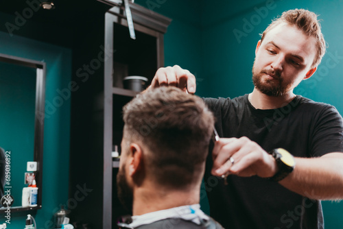 Young guy barber making haircut to client man using scissors