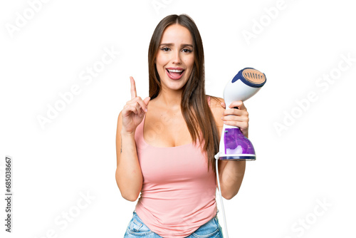 Young beautiful woman holding a vertical steam iron over isolated chroma key background pointing up a great idea