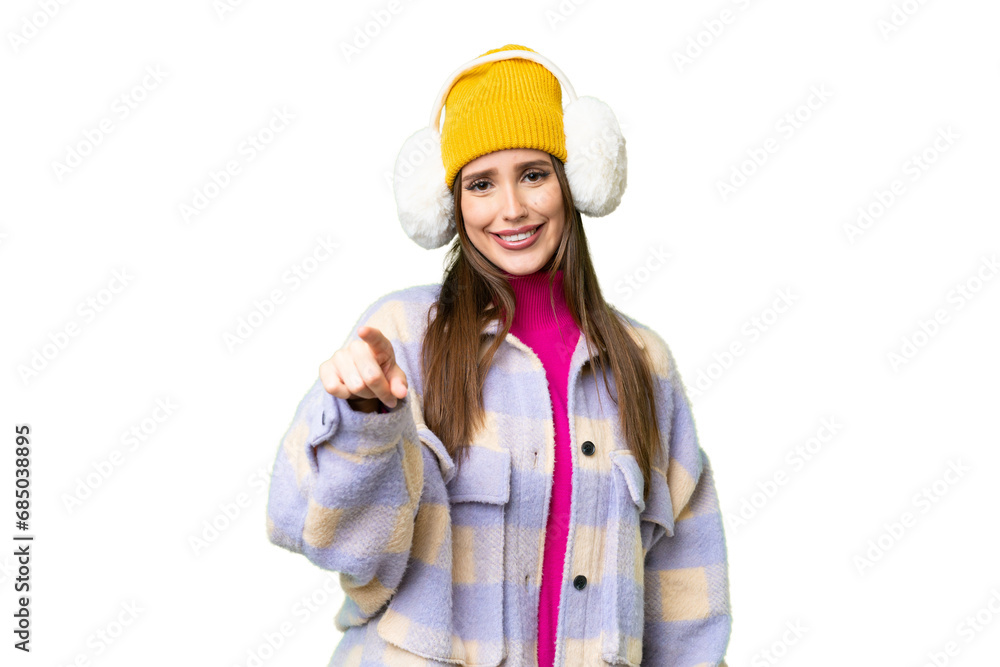 Young woman wearing winter muffs over isolated chroma key background points finger at you with a confident expression Young woman wearing winter muffs over isolated chroma key background points finger at you with a confident expression