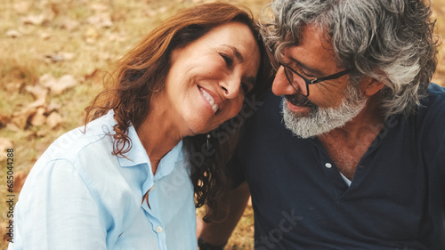 Close-up of happy retired couple spending time together, smiling and relaxing while sitting on the grass in the park in autumn