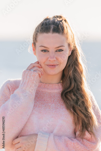 Woman with hand touching face standing in sunny daylight near sea