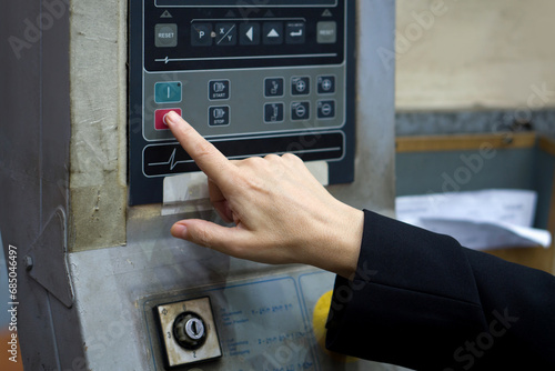 A closeup image shows a person's hand confidently pressing a specific button on a complex, detailed machine.