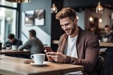 Happy male student sitting in a coffee shop, using a smartphone