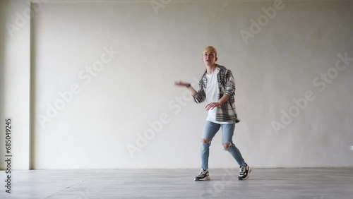 Laughing young man dancer in casual dancing in front of wall. People emotions lifestyle concept. Mock up copy space.