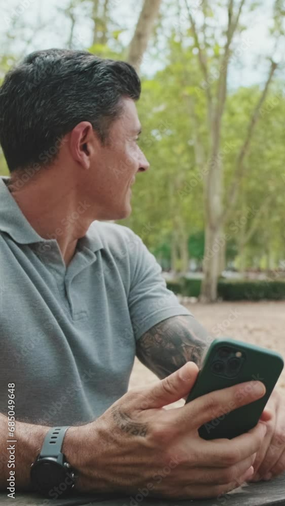 Man holding phone while sitting on park bench greets his family Man holding phone while sitting on park bench greets his family
