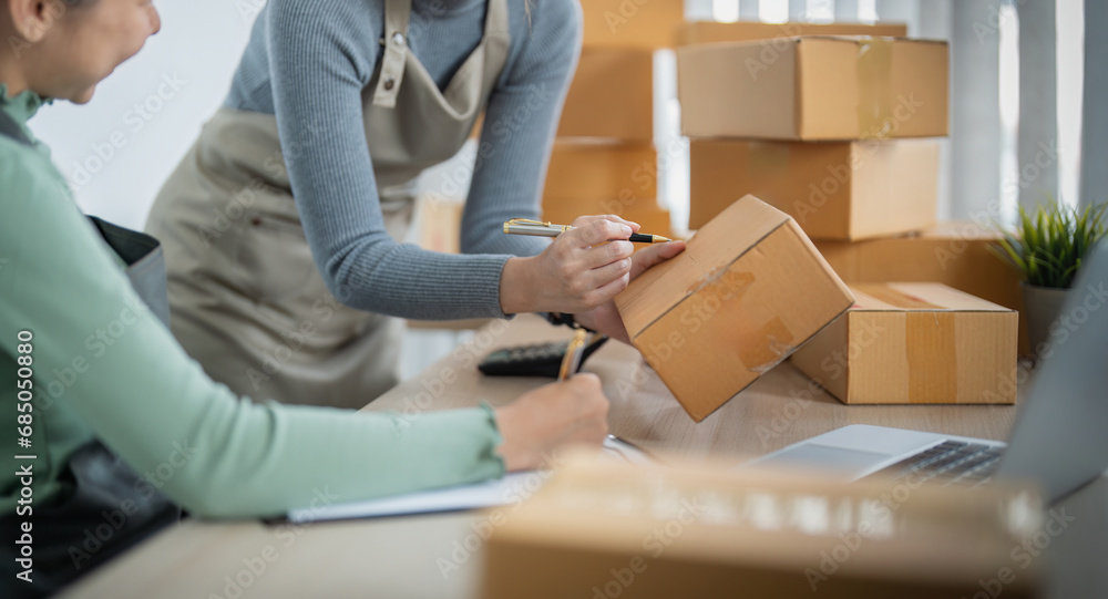 Startup small business owner working with computer at workplace. Two woman sell check product order. Packing goods for delivery to customer. Online selling. Ecommerce. Online Shopping Startup small business owner working with computer at workplace. Two woman sell check product order. Packing goods for delivery to customer. Online selling. Ecommerce. Online Shopping
