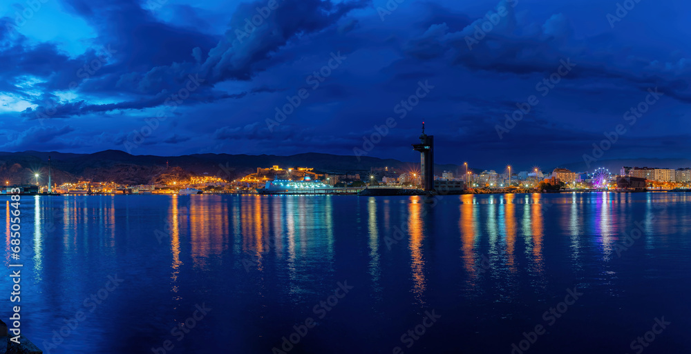 night view of the port of Almeria city with fantastic reflections of different colors in the water , during the blue hour and an illuminated Ferris wheel next to the English cable.