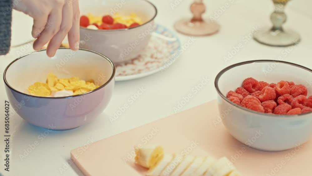 Hand placing cornflakes in a bowl with yogurt, a healthy breakfast setup. Hand placing cornflakes in a bowl with yogurt, a healthy breakfast setup.