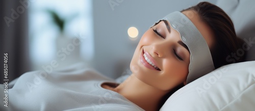 Funny young woman in grey nightwear smiling while lying in bed with an open eye mask at home copy space image