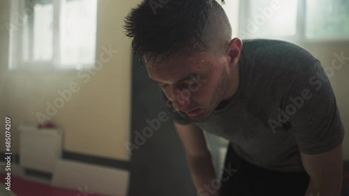 Tired male athlete with sweat on face breathes deeply resting after long boxing session in basement of gym. Exhaustion and fatigue after exercise