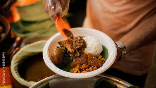 Fotografie A man serves customers gudeg rice and side dishes, a typical Yogyakarta gudeg fo