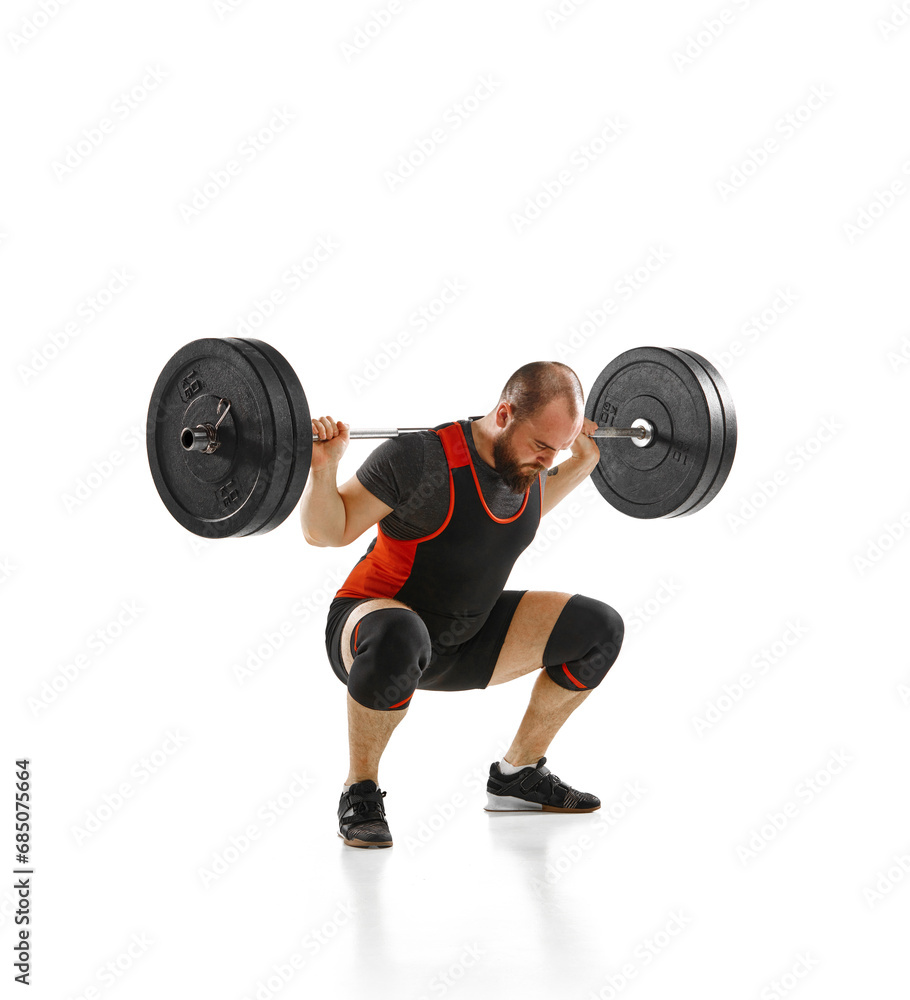 Muscular, strong young athlete, bodybuilder doing squats and lifting barbell, heavy weights against white background Muscular, strong young athlete, bodybuilder doing squats and lifting barbell, heavy weights against white background