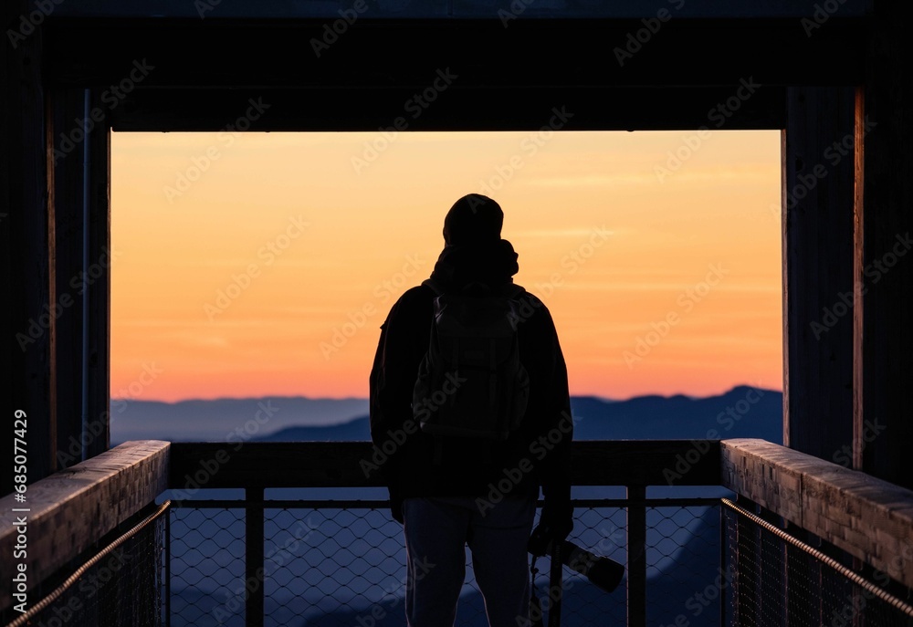 Man standing in an elevated position, gazing out over a mountainous landscape at sunset