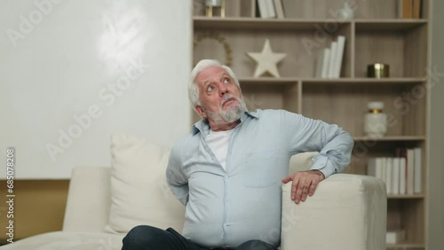 Senior man tries to stand from armchair. Elderly male suffering atherosclerosis, arthritis, osteoporosis disease. Health problems in old age, stiffness of movements, painful sensations in lower back.