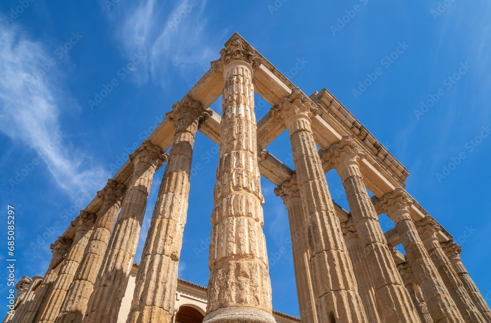 View from below with pyramidal perspective of the Roman temple of Diana with well-preserved Corinthian style marble columns under a clear blue sky. Merida. Province of Badajoz, Extremadura, Spain.