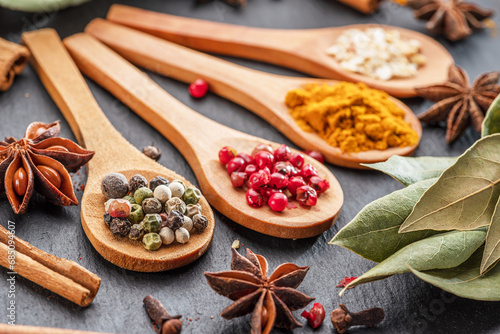 Various types of spices on wooden spoons on a gray stone table.