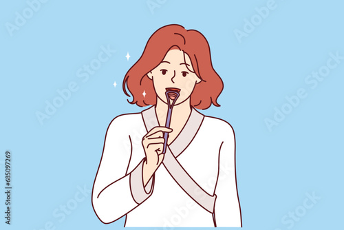 Woman uses tongue brush to clean mouth from germs, showing example of hygiene education. Girl in bathrobe brushes tongue to improve health and preventively combat formation of caries