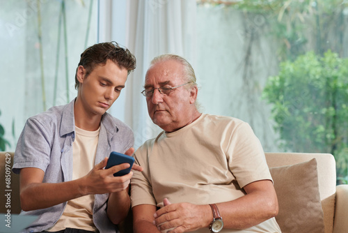 Young man showing senior man how to send text messages, voice messages and stickers in messenger