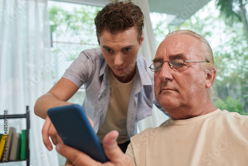 Young man helping grandfather to install dating application on smartphone